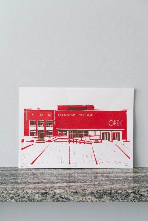 A minimalist red and white art print depicting the 'Openbar Entrepot' building, leaning against a red brick wall on a speckled gray countertop.