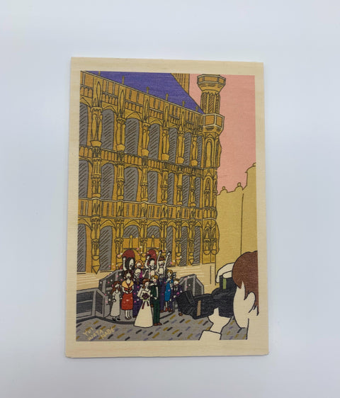 A decorative wooden accessory featuring an illustration of a newlywed couple with loved ones in front of Leuven’s historic Town Hall.