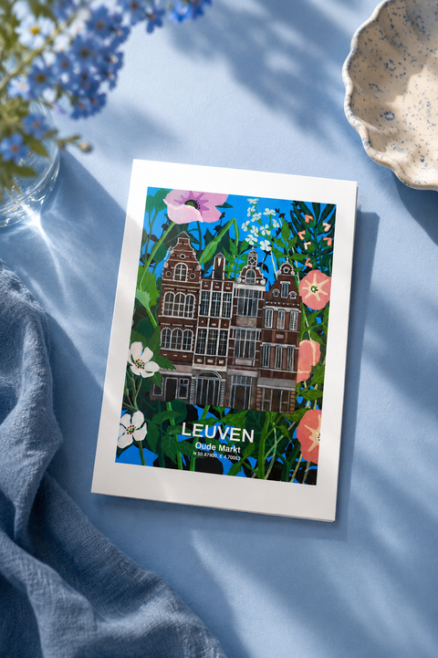 A square art print featuring a colorful illustration of Leuven,Oude Markt, styled on a light blue fabric background with a blue cloth, blue flowers, and a ceramic dish.
