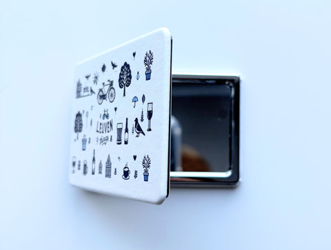 Double-sided pocket mirror with playful navy blue illustrations of Leuven icons, including bikes, trees, drinks, and architecture, and the text “Leuven things” on a light background.