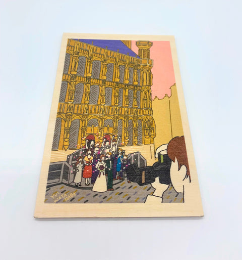 A decorative wooden accessory featuring an illustration of a newlywed couple with loved ones in front of Leuven’s historic Town Hall.