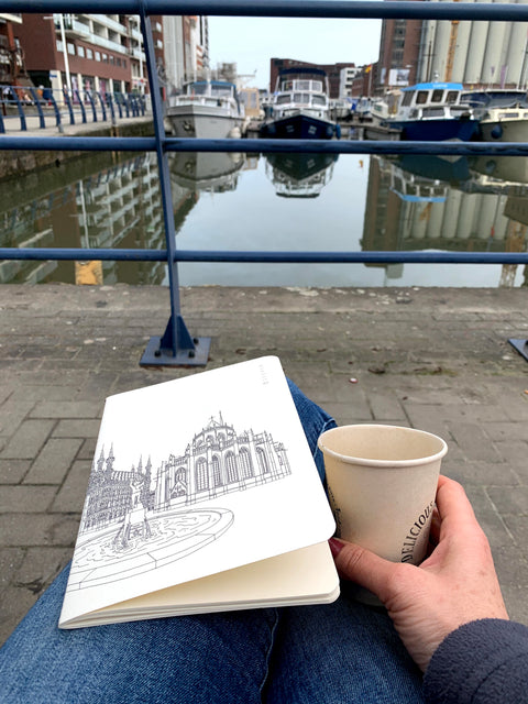 Notebook with a black line art illustration of Leuven’s Grote Markt, featuring the Town Hall, Saint Peter’s Church, and fountain on a cream-colored cover.