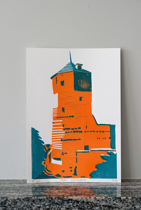 A vertical art print featuring a stylized orange and teal tower illustration on a white sheet, leaning against a red-brown brick wall on a speckled stone surface