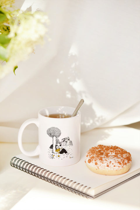 White ceramic mug featuring a whimsical black-and-yellow illustration of a girl relaxing under a tree near Leuven’s City Park, with a coffee bottle and book by her side.