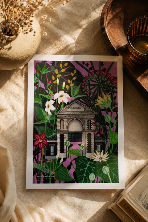 A botanical art print featuring a classical building labeled 'Kruidtuin' surrounded by lush green leaves and pink, white, and yellow flowers, styled on a beige fabric surface with dried flowers, a wooden tray, and a book.