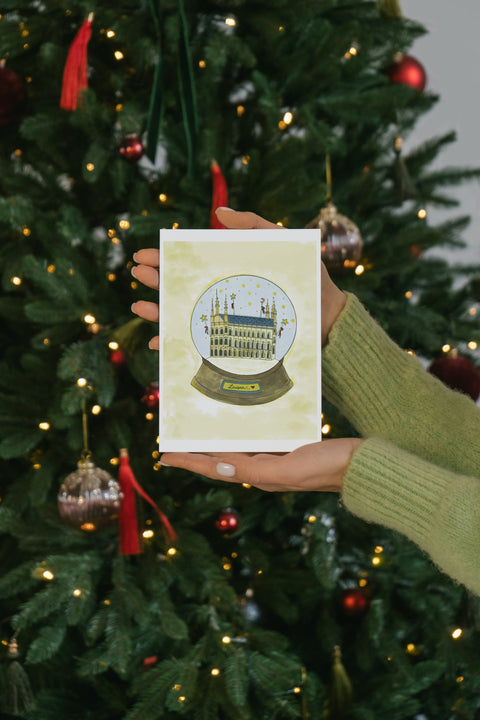 A beautifully illustrated postcard featuring Leuven’s Historical City Hall inside a snow globe, part of a popular series combining natural beauty with stars and angels. Printed on premium paper, includes a matching envelope—perfect for mailing, gifting, or collecting as a charming Leuven souvenir.