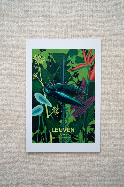 A rectangular art print with a white border lies on a wooden surface. The print features a colorful illustration of a TOTEM in dark green leaves and red flowers, with the word 'LEUVEN' and smaller text near the bottom.